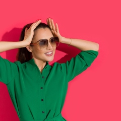 Beautiful young woman in elegant sunglasses is posing on red wall.