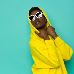 Black woman in yellow hoodie and sunglasses looking up