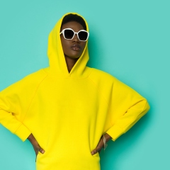 Seriosu black woman in sunglasses and vibrant yellow hooded sweatshirt.