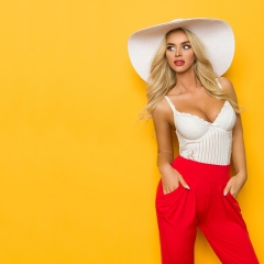 Sexy Blond Woman In White Sun Hat, Corset And Red Trousers Is Looking Away