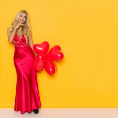 Smiling Beautiful Woman In Elegant Red Dress Is Holding Heart Shaped Balloons And Looking Away
